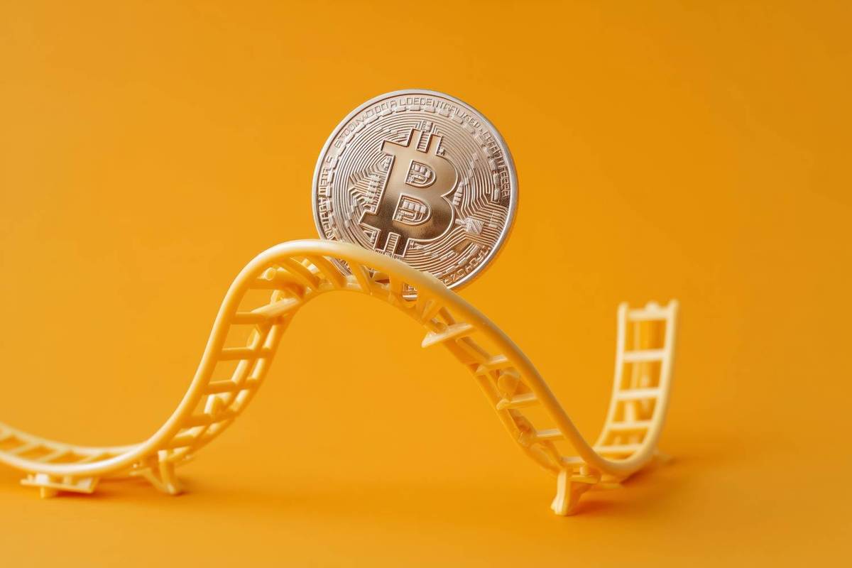 A Bitcoin coin rests on a miniature yellow roller coaster track against an orange background; text reads: "Bitcoin".
