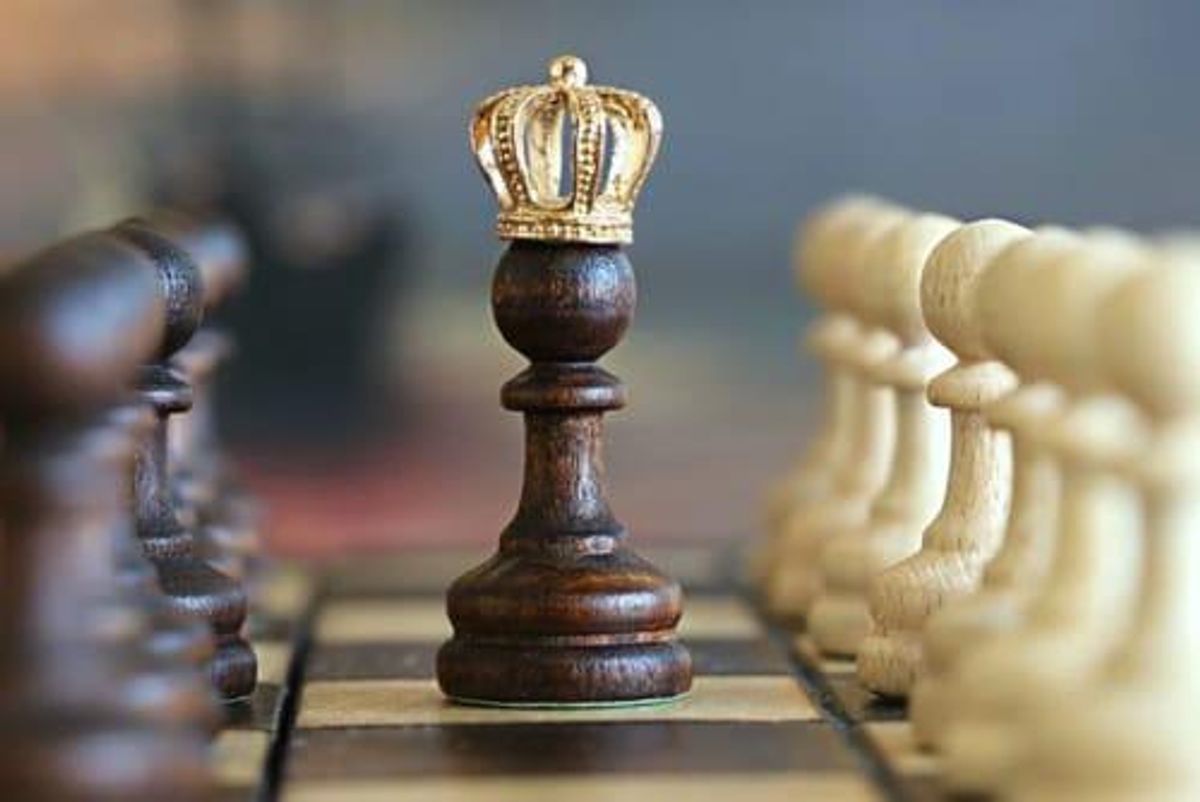 a black pawn with a small crown on top of it sits on a chess board between rows of pawns