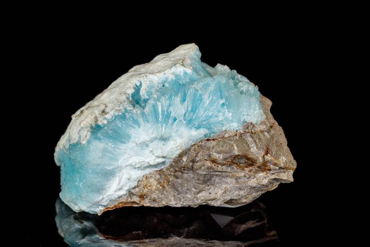 A blue and white mineral rock containing cobalt with rough texture sits on a reflective black surface.