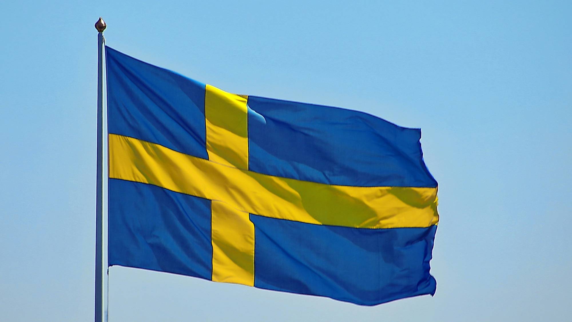 A blue flag with a yellow cross flies against a clear sky.