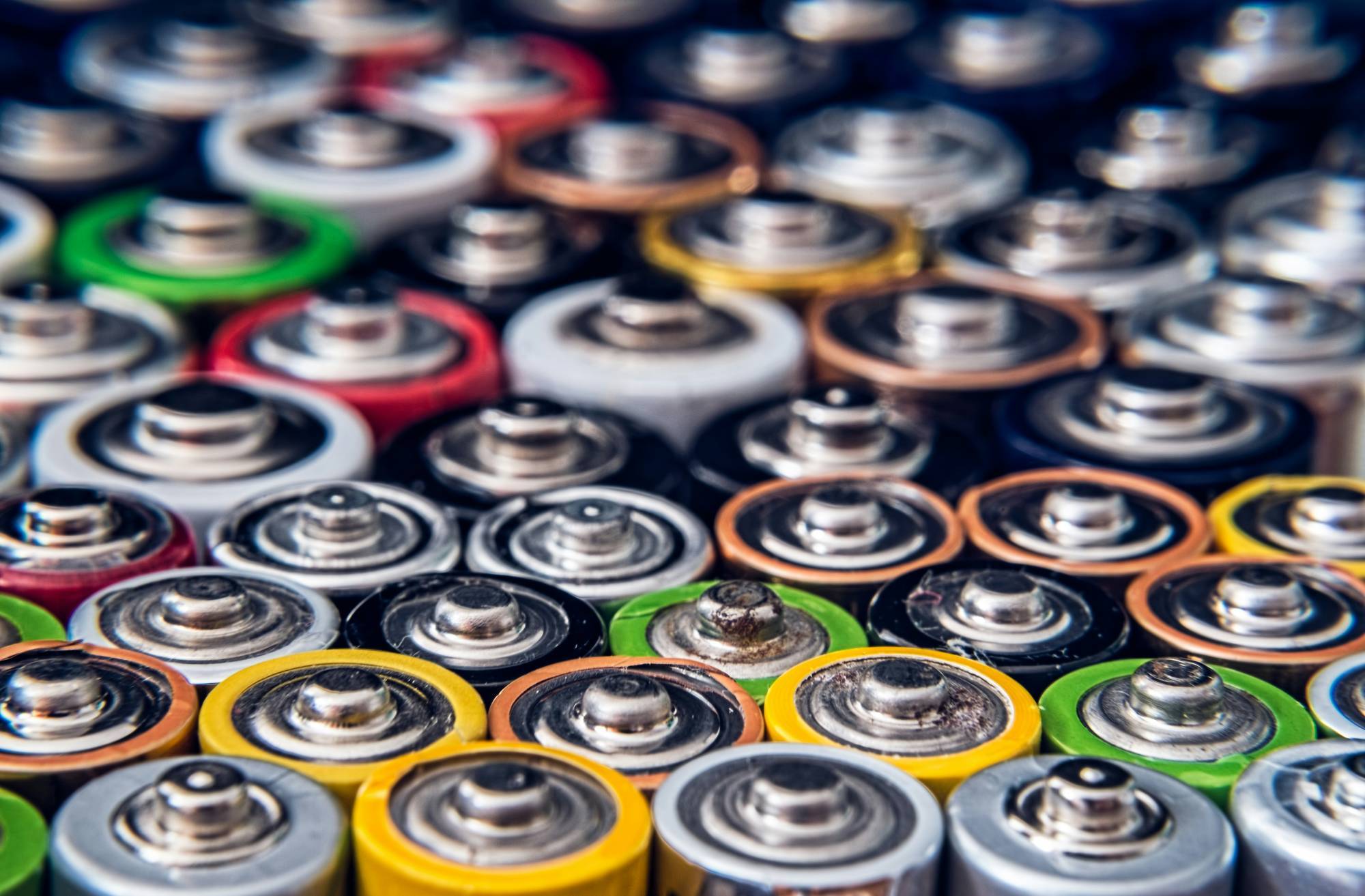 A close-up of assorted colorful battery tops, including green, red, yellow, and silver, closely packed together.