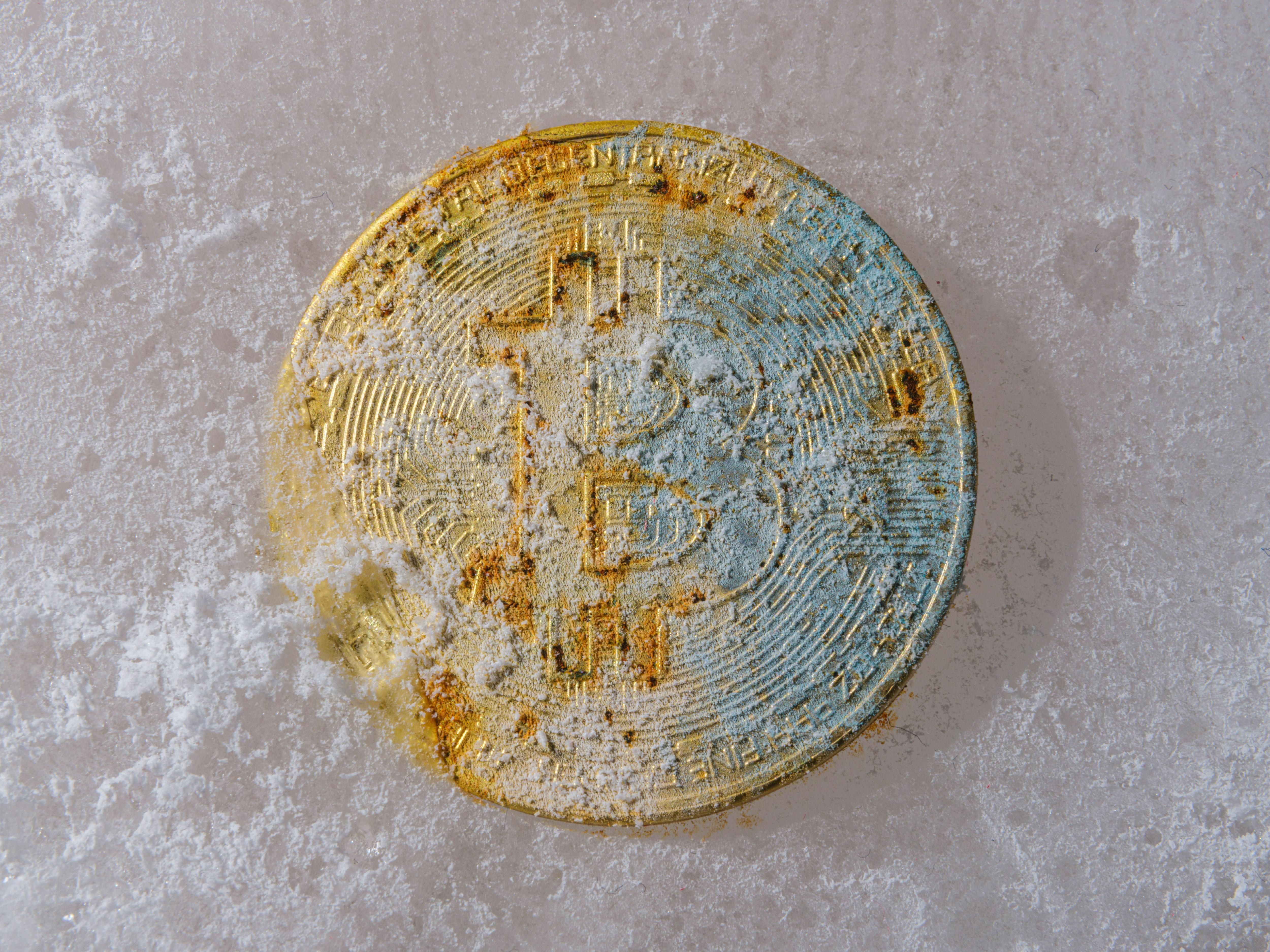 A frosty, weathered Bitcoin coin on a snow-covered surface.