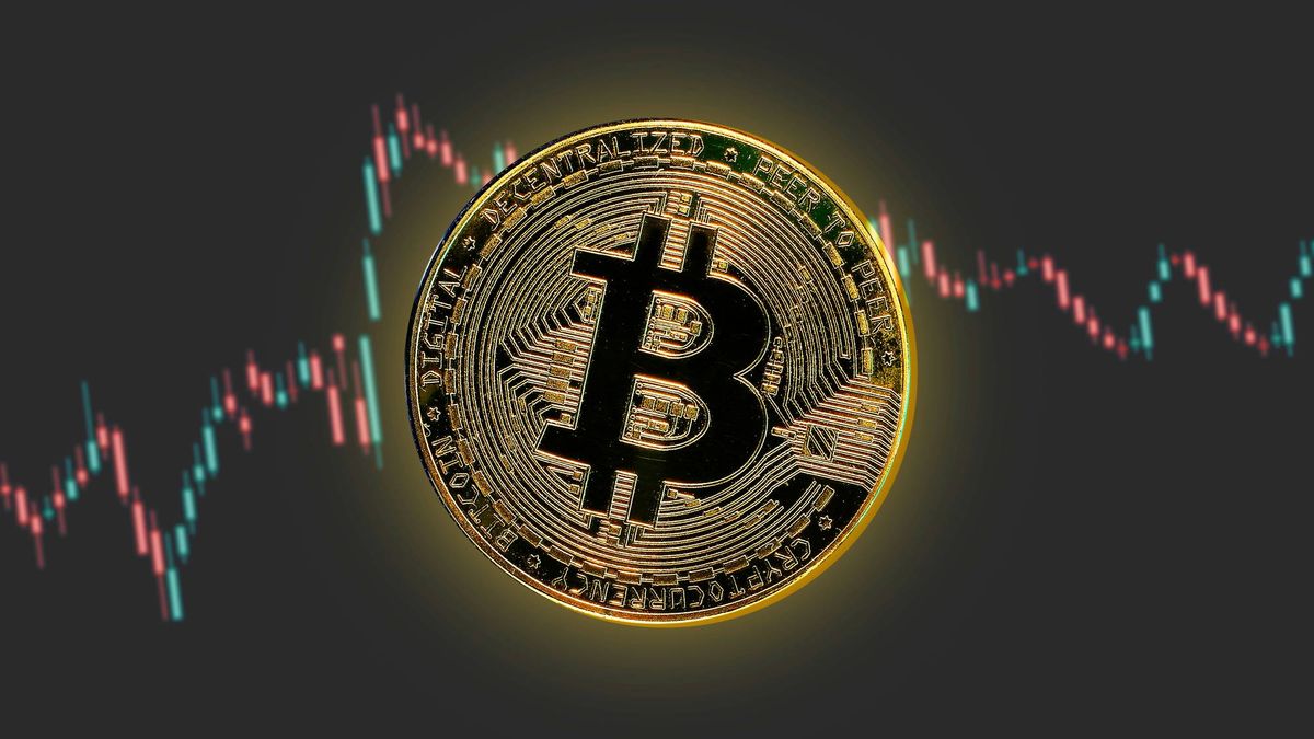 A glowing Bitcoin coin is centered over a gray background with fluctuating red and blue candlestick charts.