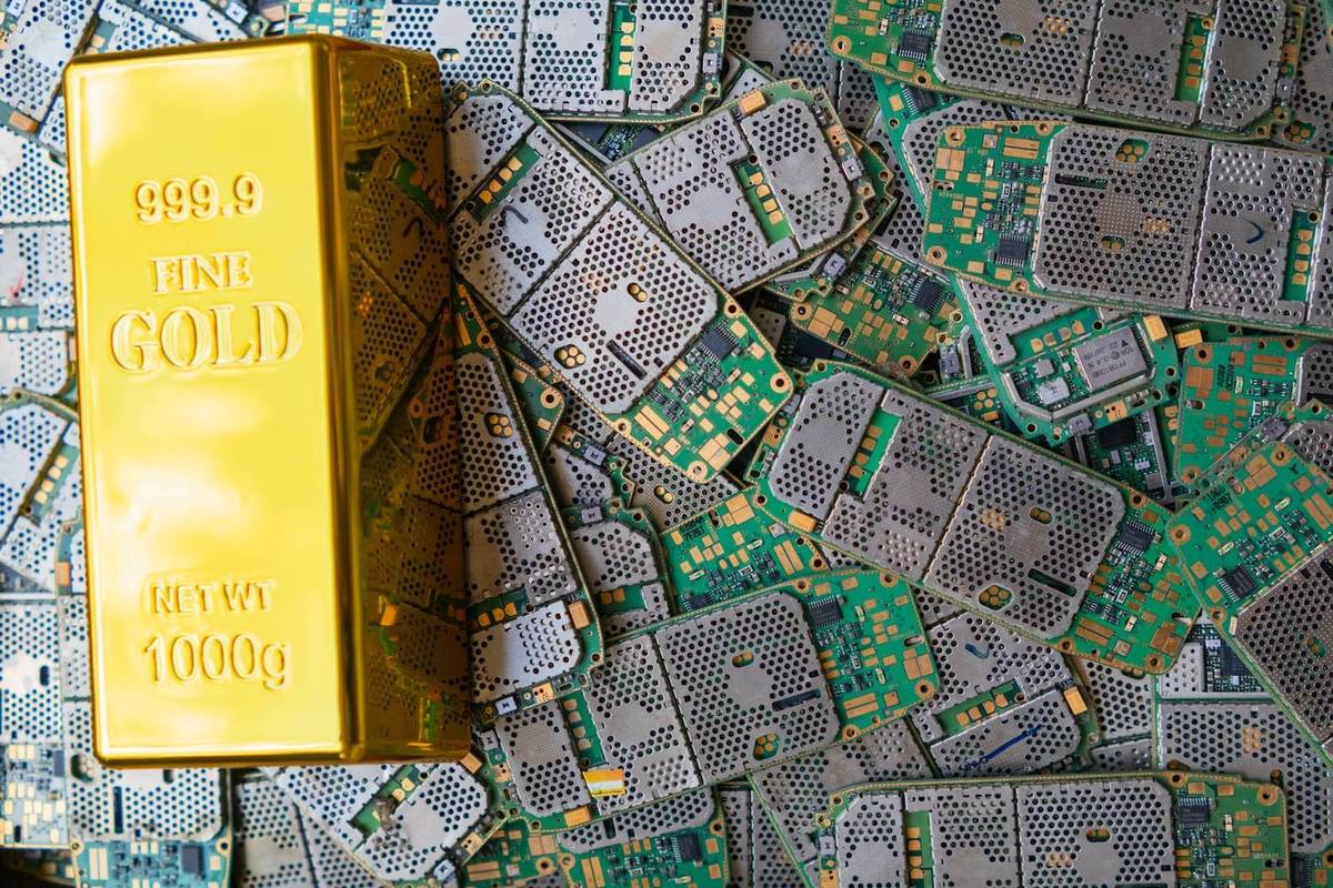 A gold bar with text stands over a background of green and silver circuit boards. Text reads: 999.9 FINE GOLD NET WT 1000g.