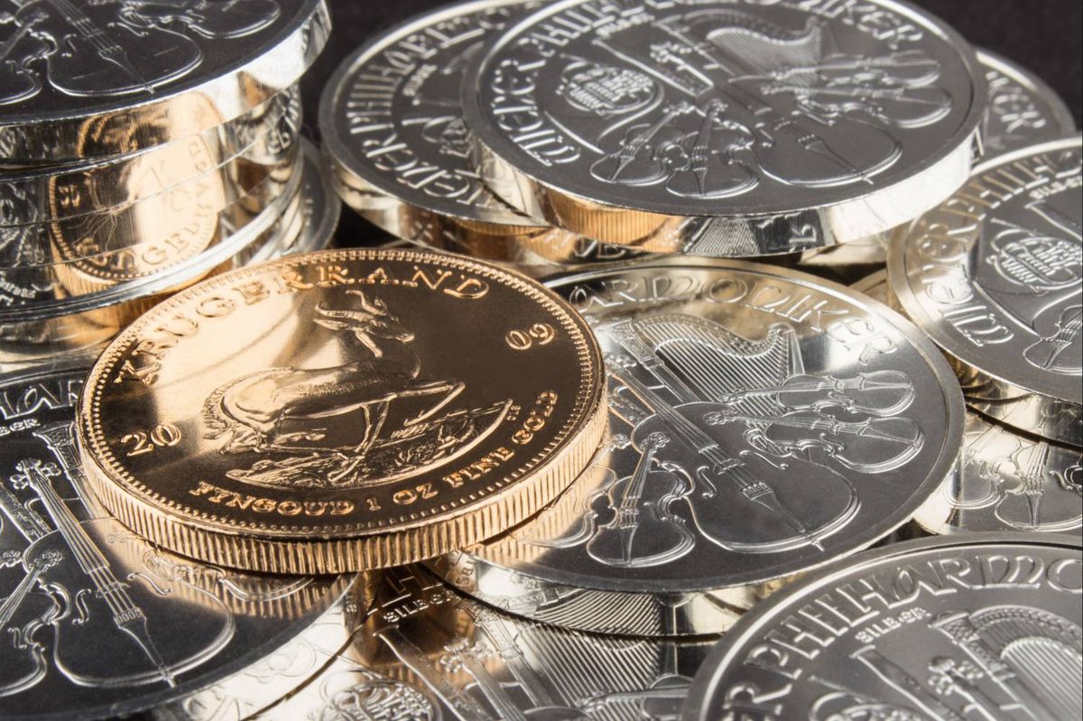 A gold Krugerrand coin sits atop a pile of silver coins with musical instrument engravings.