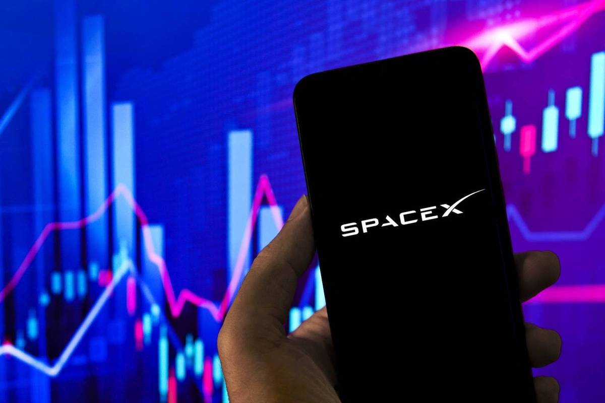 A hand holding a phone displaying SpaceX logo over a colorful financial graph background.