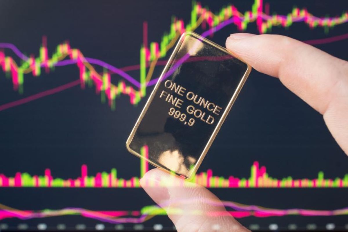 a hand holding a small gold bar in front of stock screen