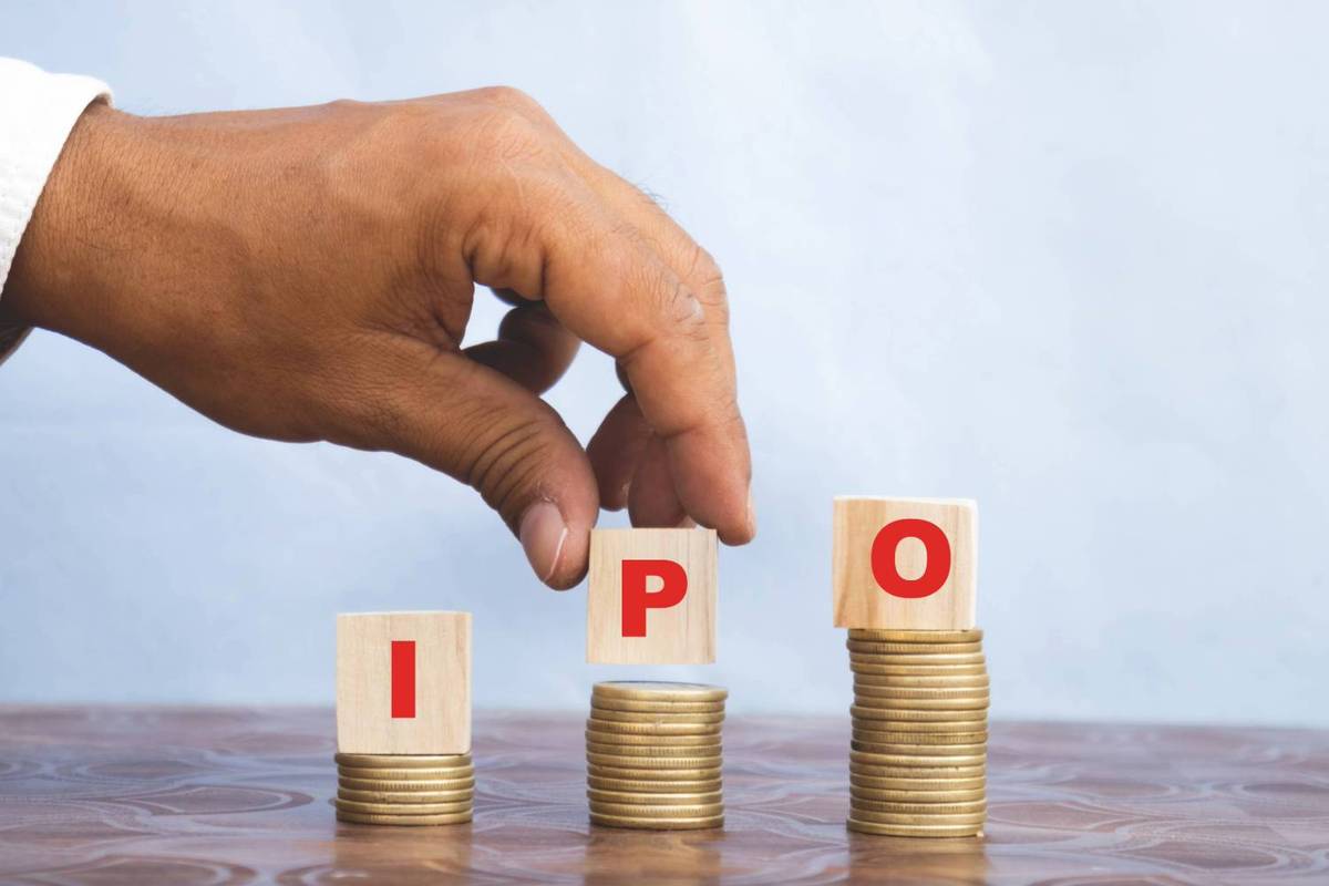 A hand places wooden blocks with "IPO" over stacks of coins on a wooden surface, light blue background.