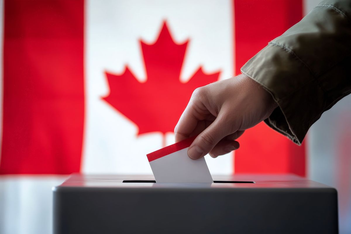 A hand puts a ballot in a ballot box in front of Canadian flag.