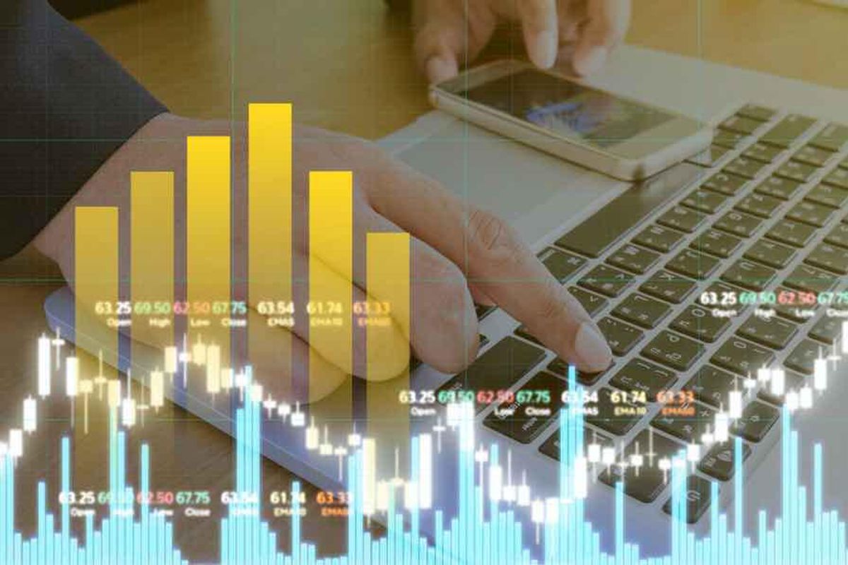 a hand typing on a laptop amid stock information