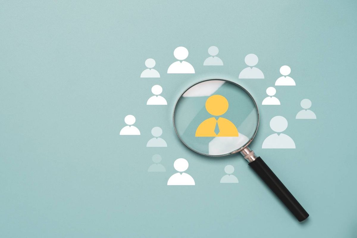 A magnifying glass highlights a yellow figure among white figures on a textured teal background.