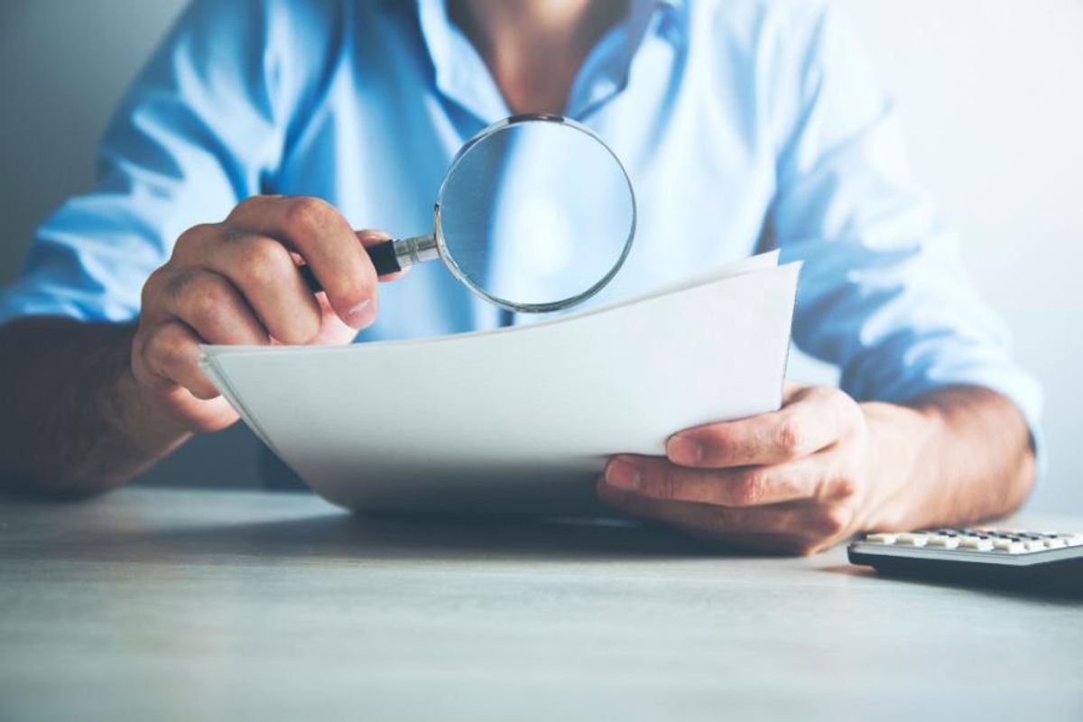 a man holds stack of papers and a magnifying glass