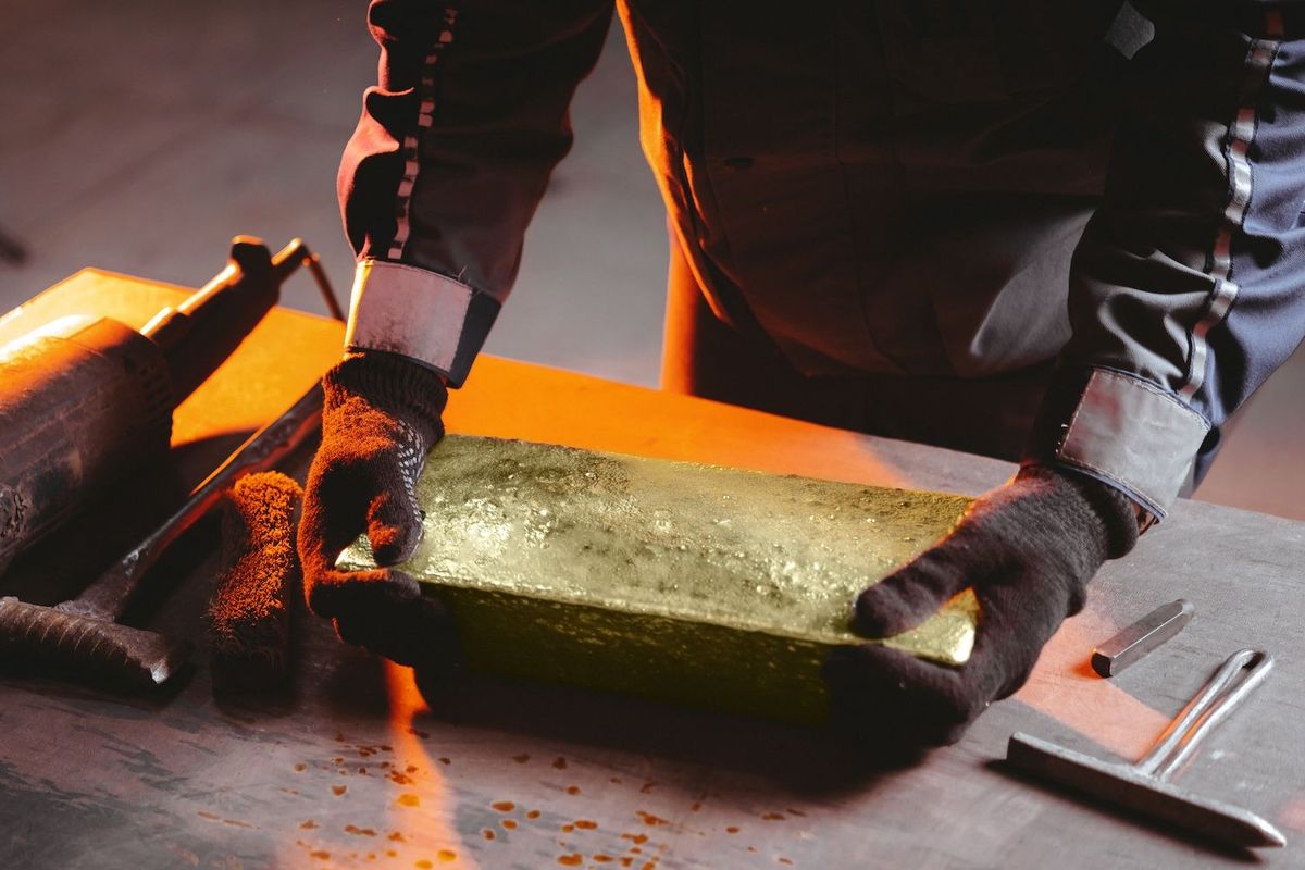 A metal worker wear gloves and holding a gold ingot.
