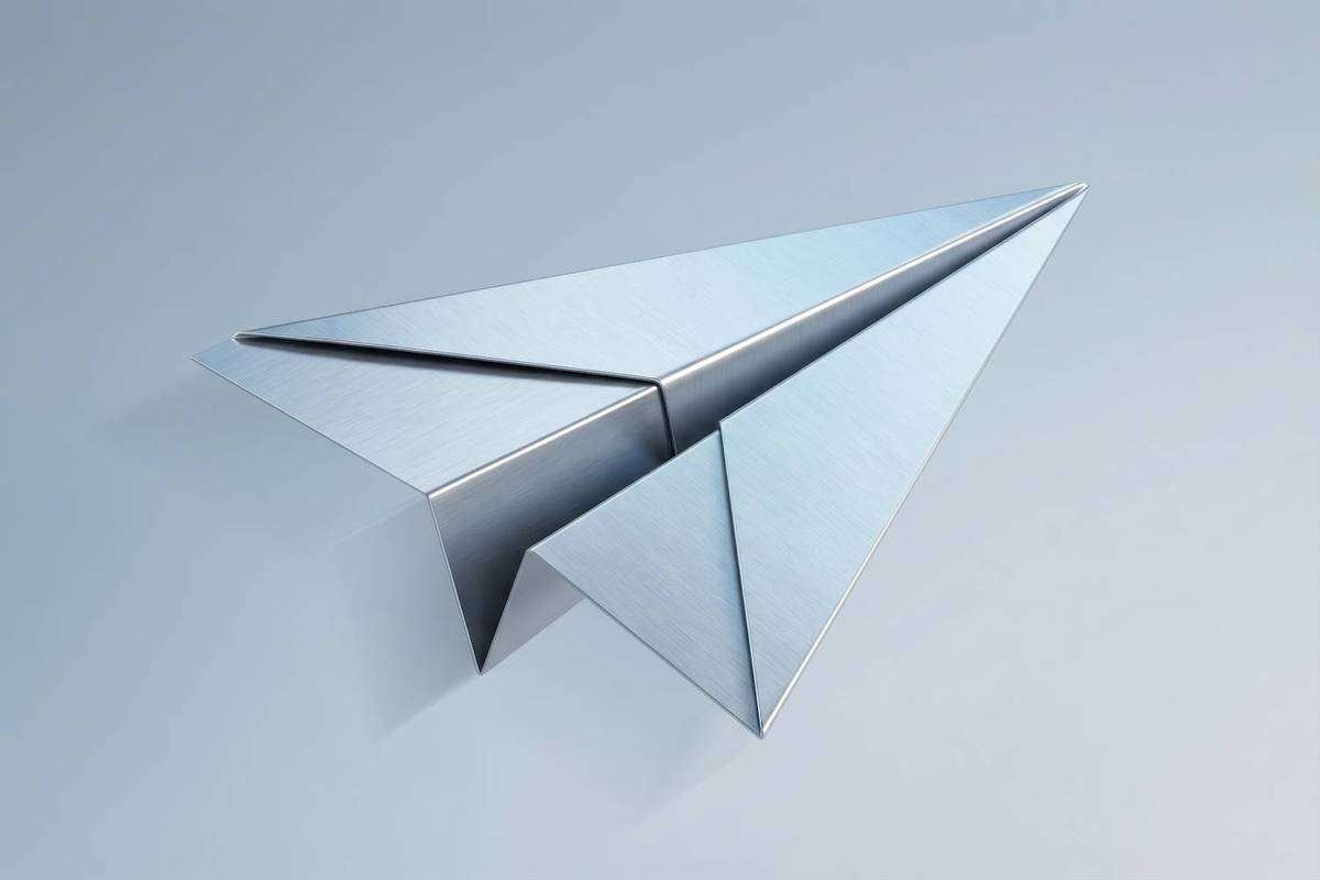 A metallic paper airplane rests on a smooth light gray surface.