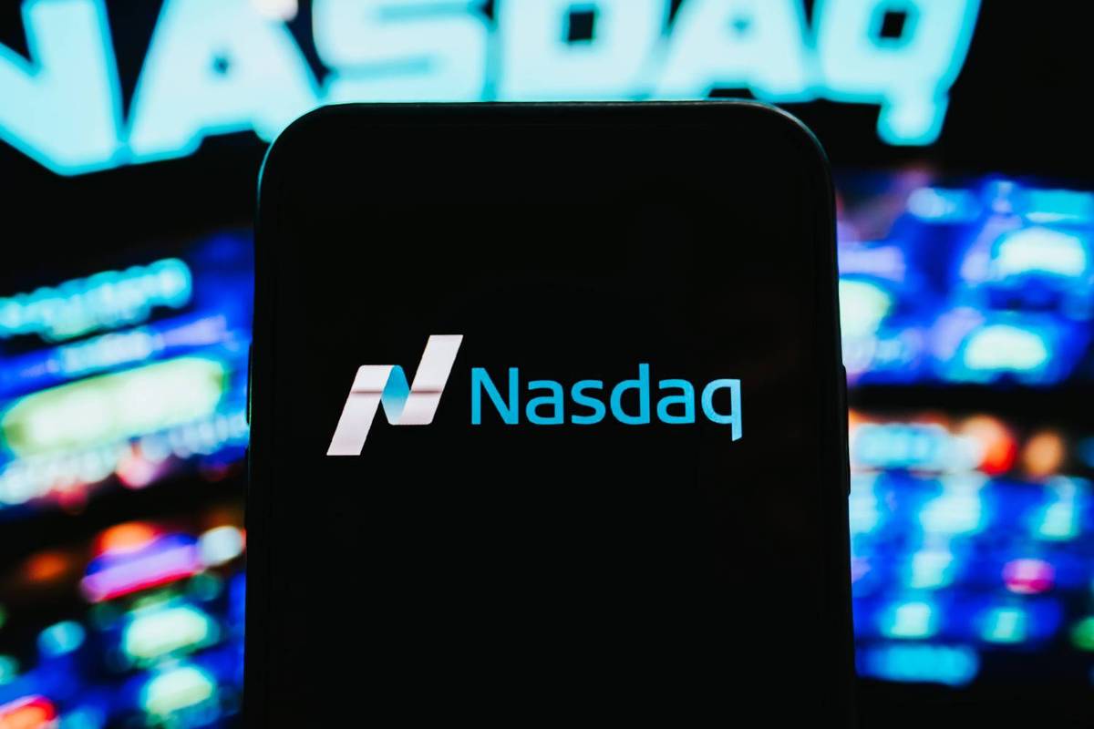 A phone displaying "Nasdaq" in front of a blurred, neon-lit Nasdaq sign and colorful screens.