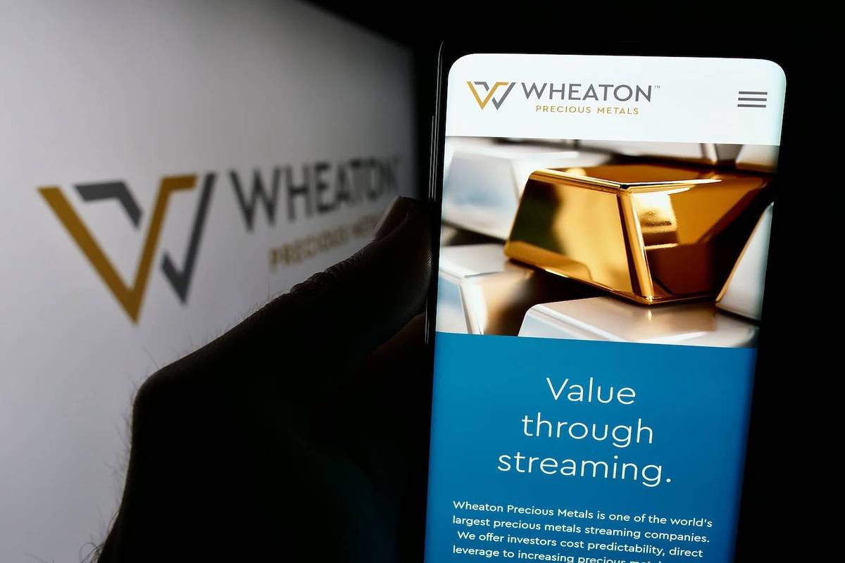 A phone displaying Wheaton Precious Metals website with gold bars on screen; logo and text in background.