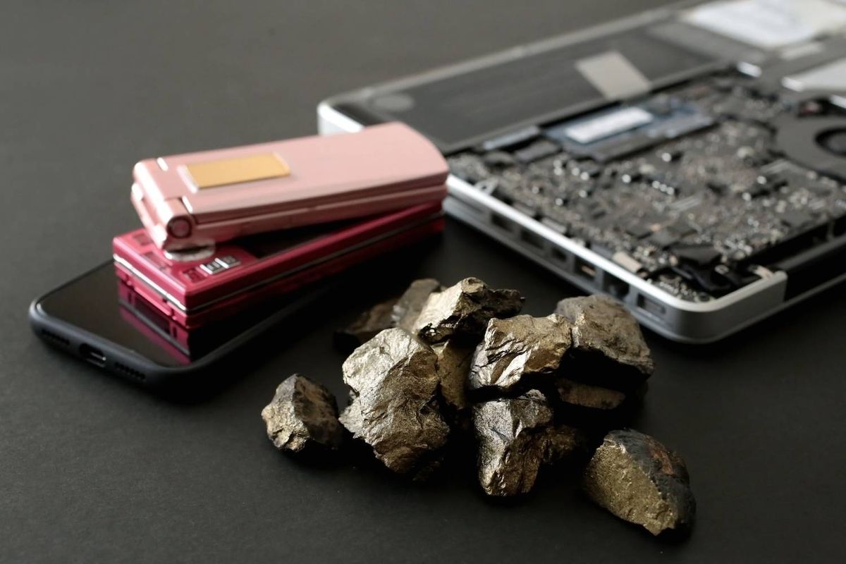 A pile of metallic rocks in front of a laptop and stacked flip phones on a black surface.