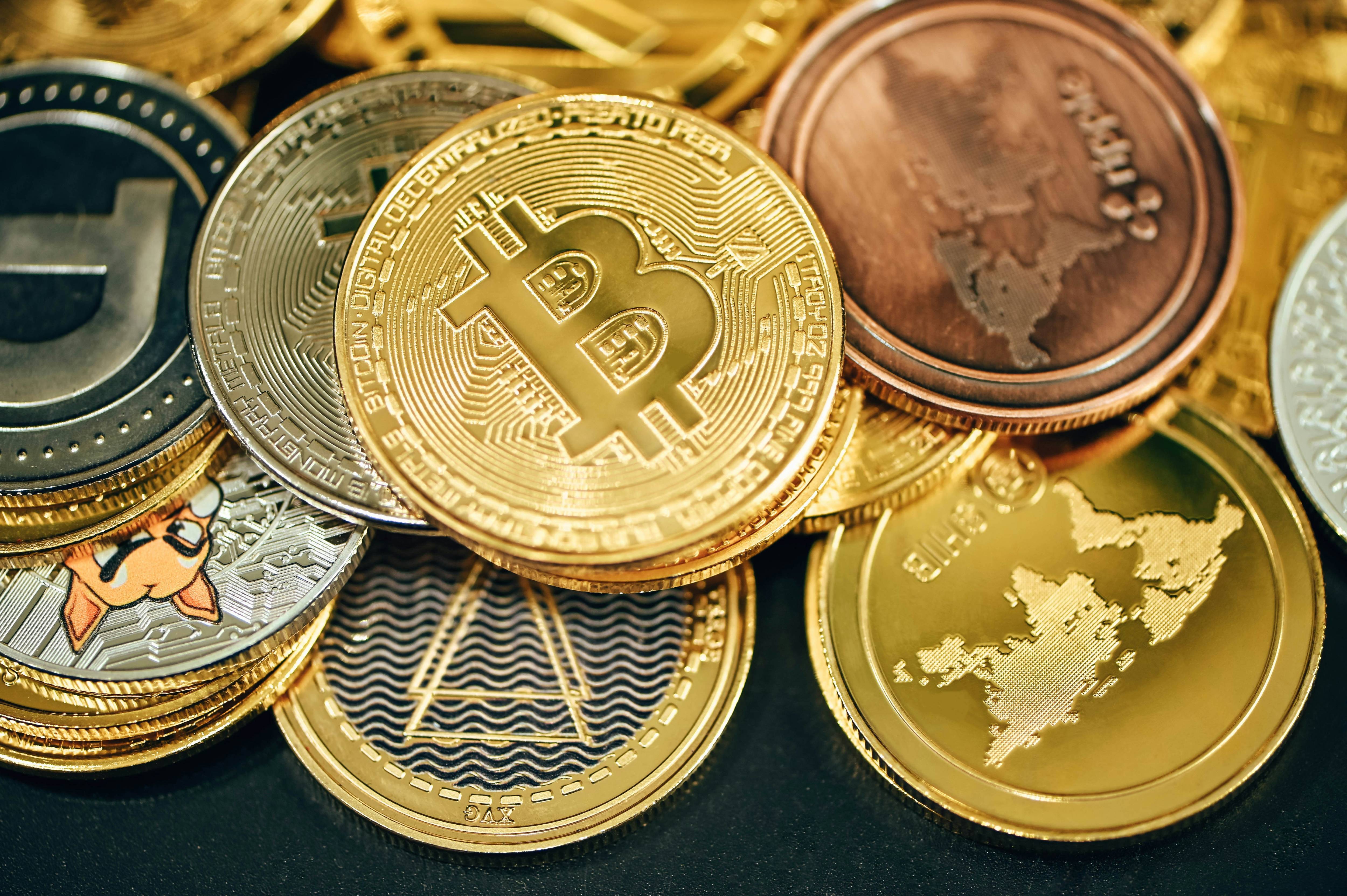 A pile of various metallic cryptocurrency coins, featuring Bitcoin, with intricate designs and a world map.