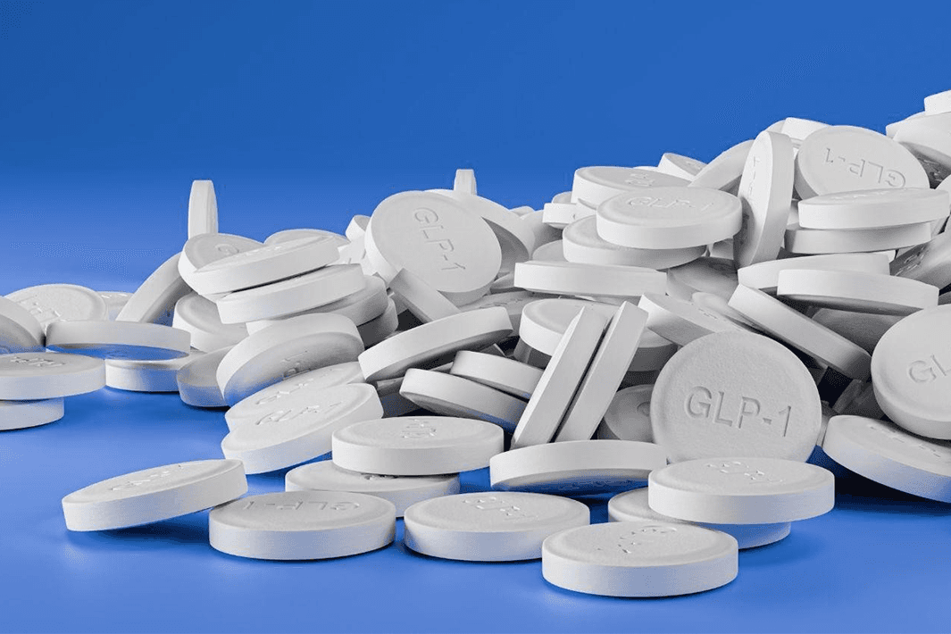 A pile of white round GLP-1 tablets on a blue surface.