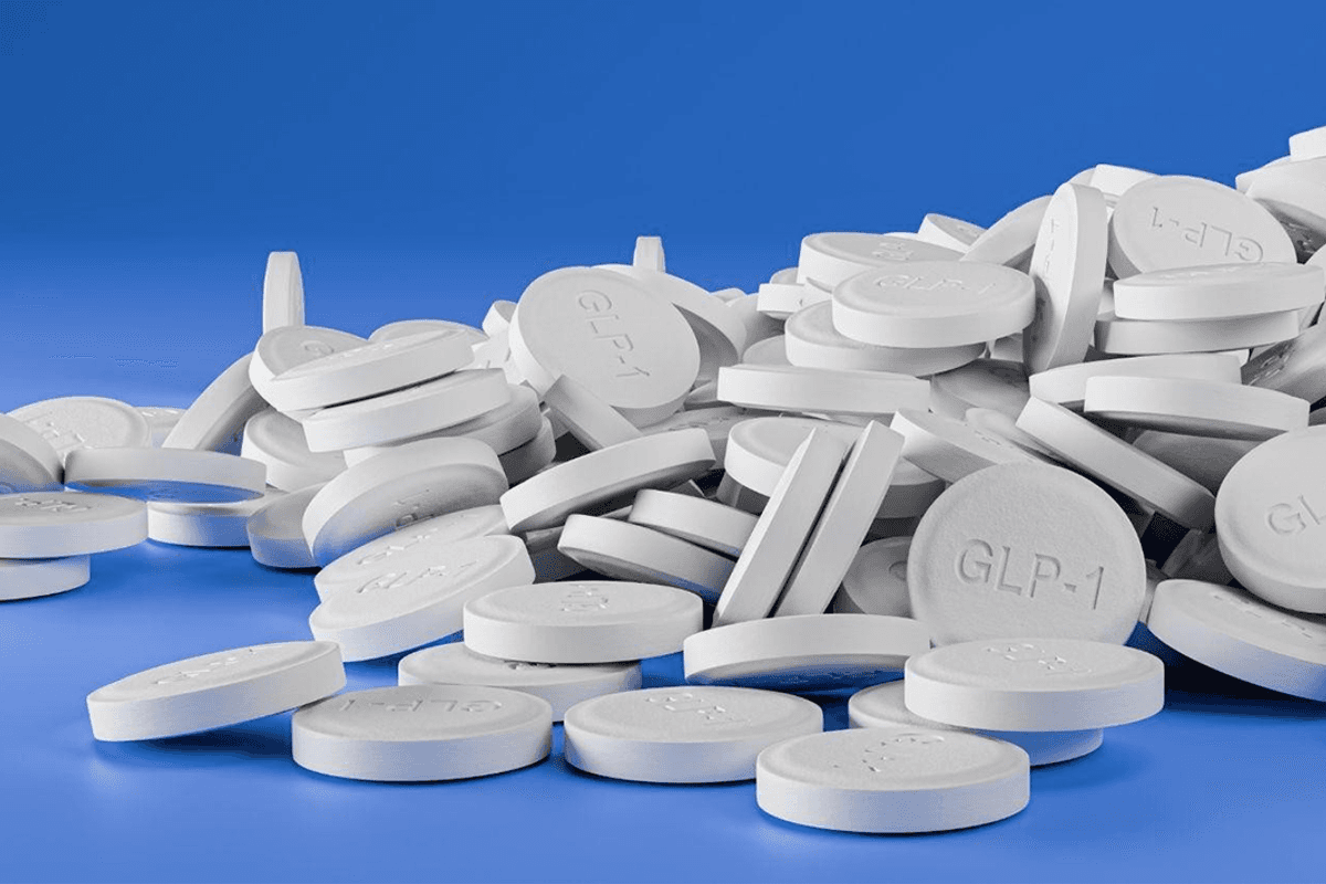 A pile of white round GLP-1 tablets on a blue surface.
