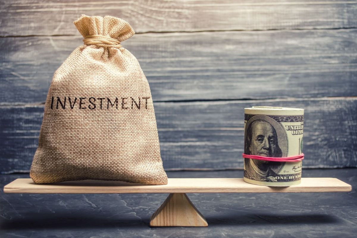 A sack labeled "Investment" and rolled money balanced on a wooden plank.