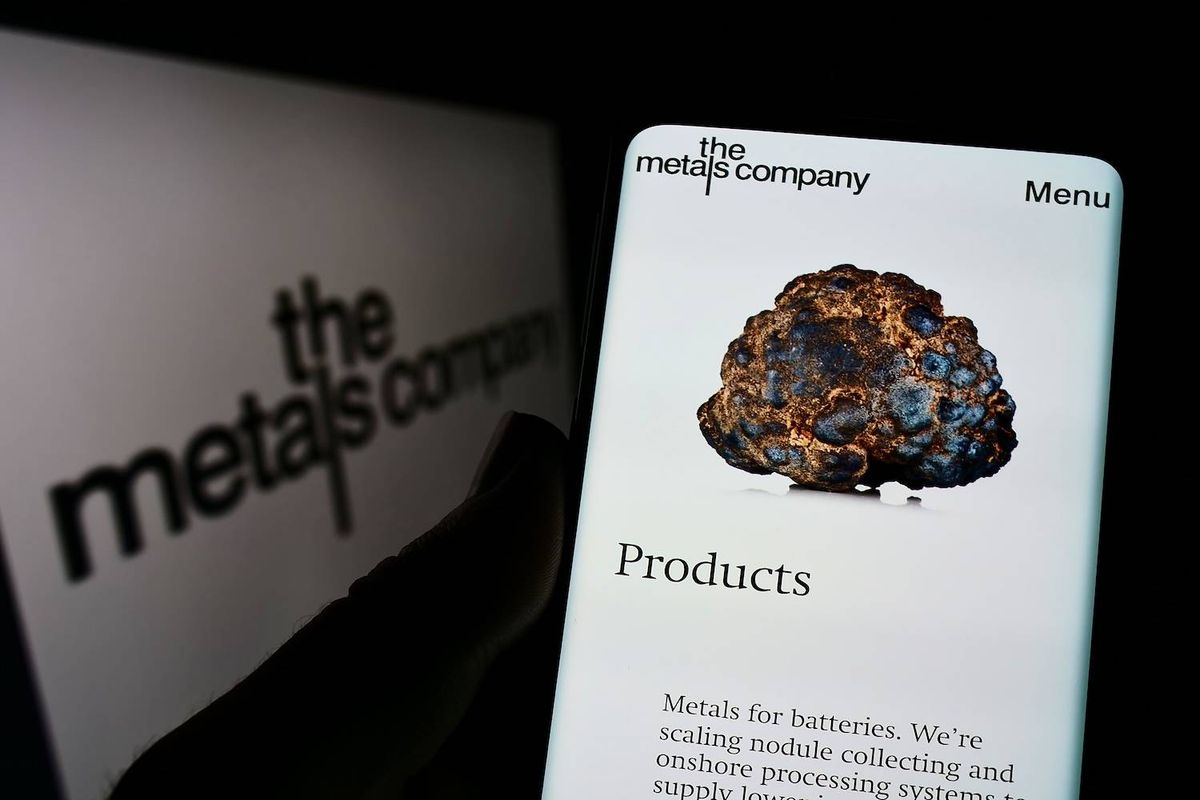 A smartphone displays a metallic nodule image and text while a blurred logo is in the background.