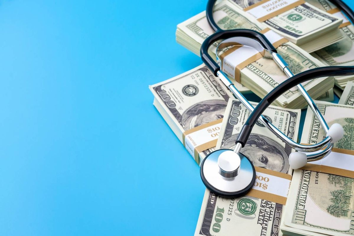 A stethoscope rests on stacks of US dollar bills over a bright blue background.