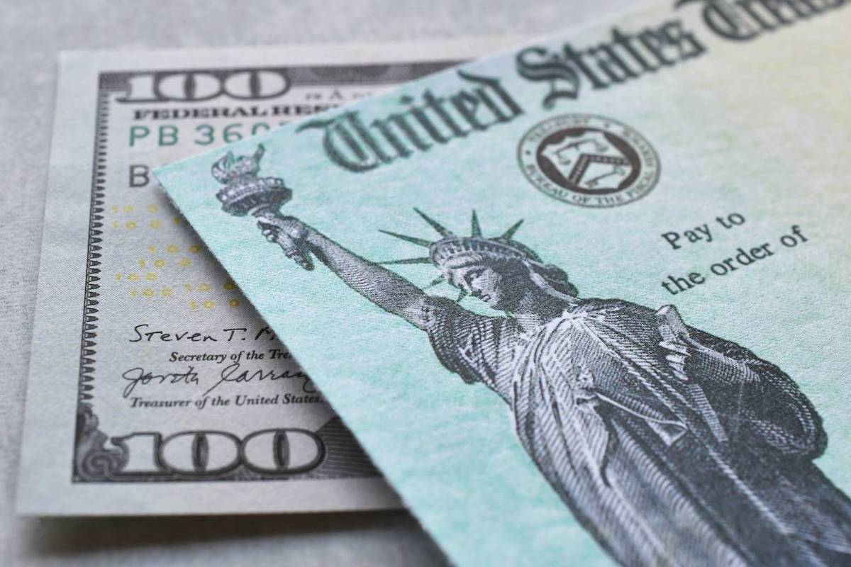 A U.S. Treasury check with the Statue of Liberty is placed over a one hundred dollar bill.