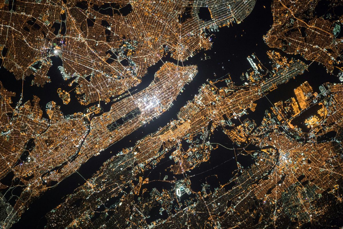 Aerial view of a brightly lit cityscape at night, with glowing street patterns and waterways.
