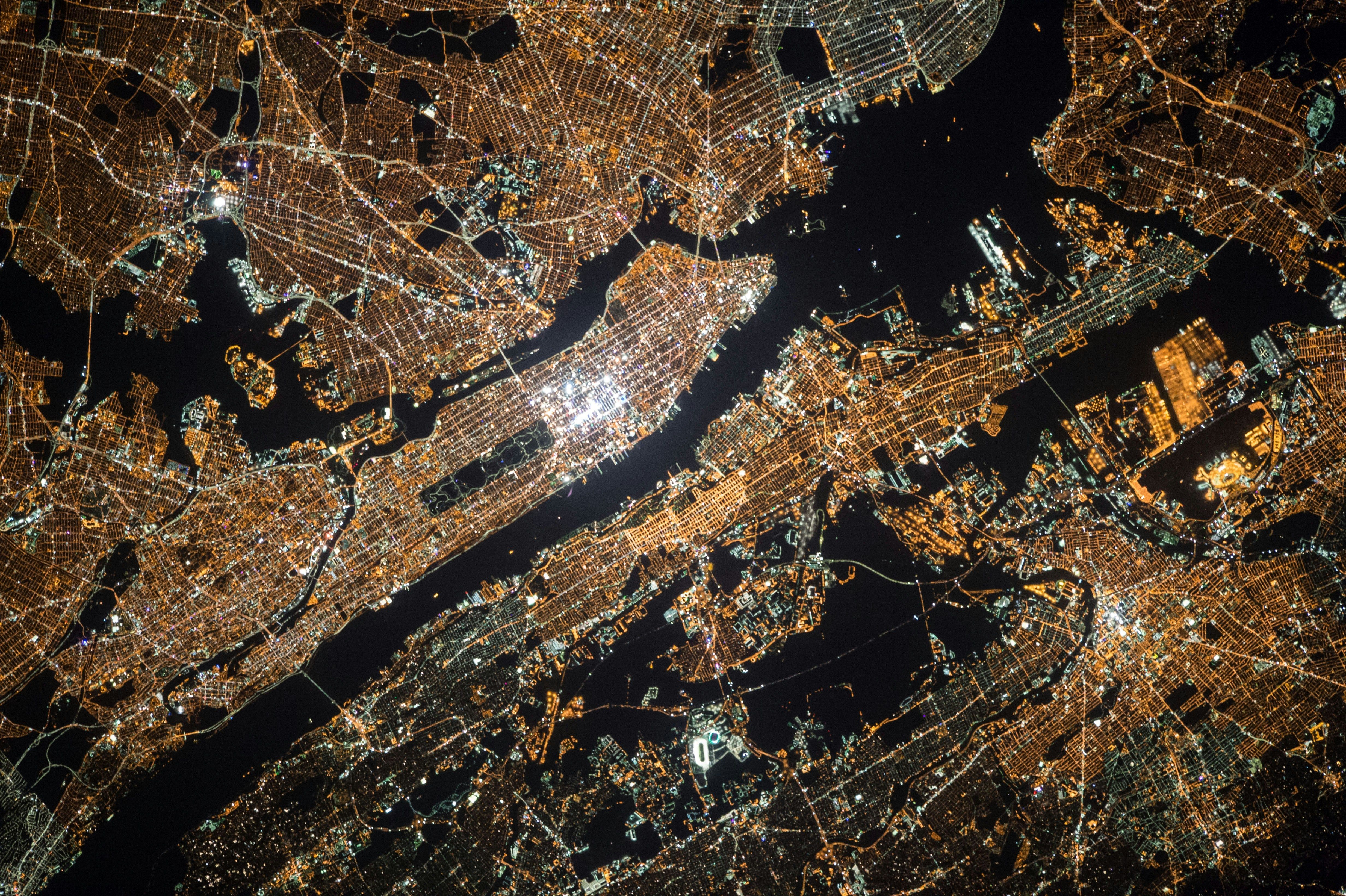 Aerial view of a brightly lit cityscape at night, with glowing street patterns and waterways.