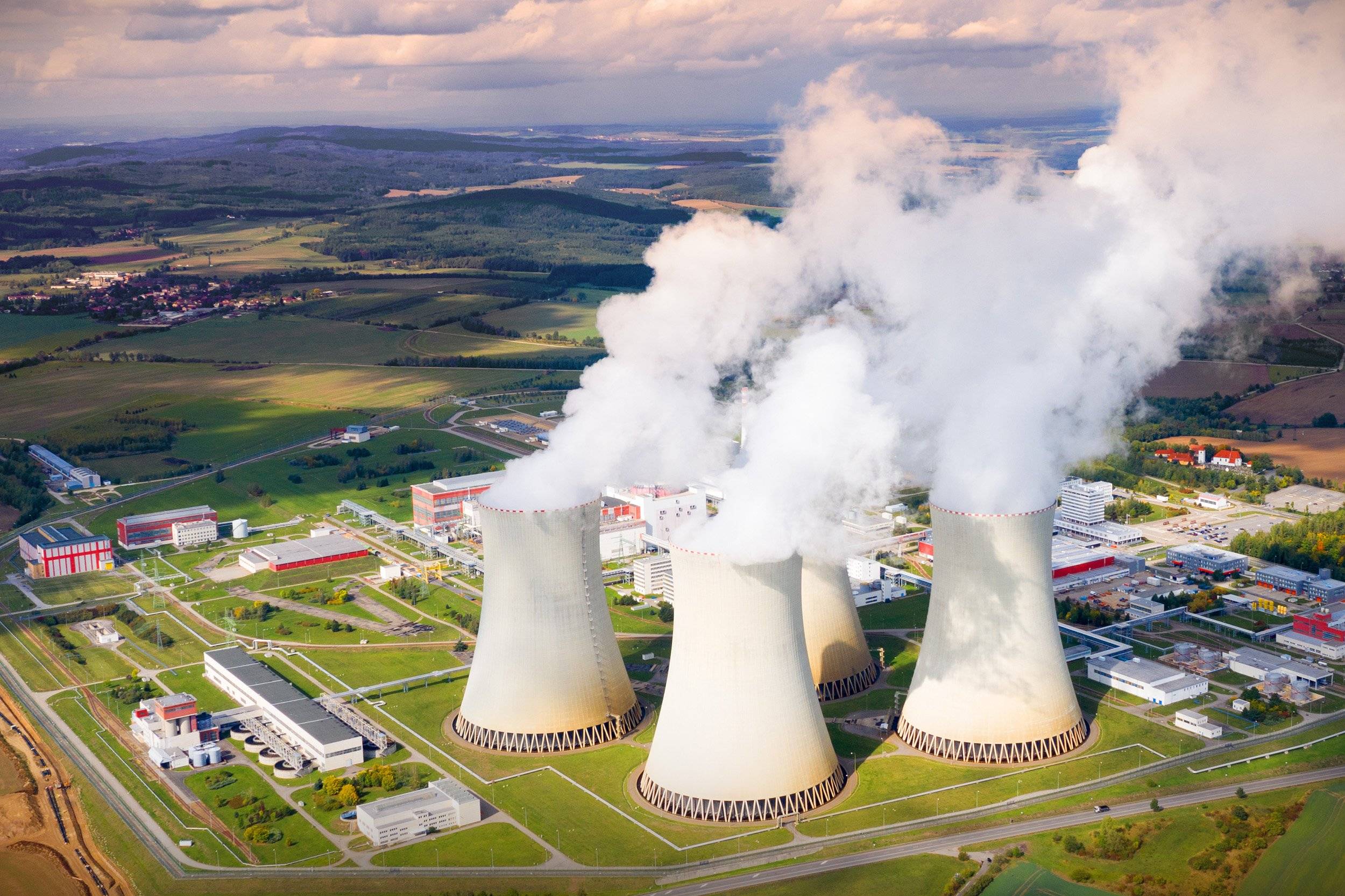Aerial view of a nuclear power plant with four large cooling towers emitting steam.