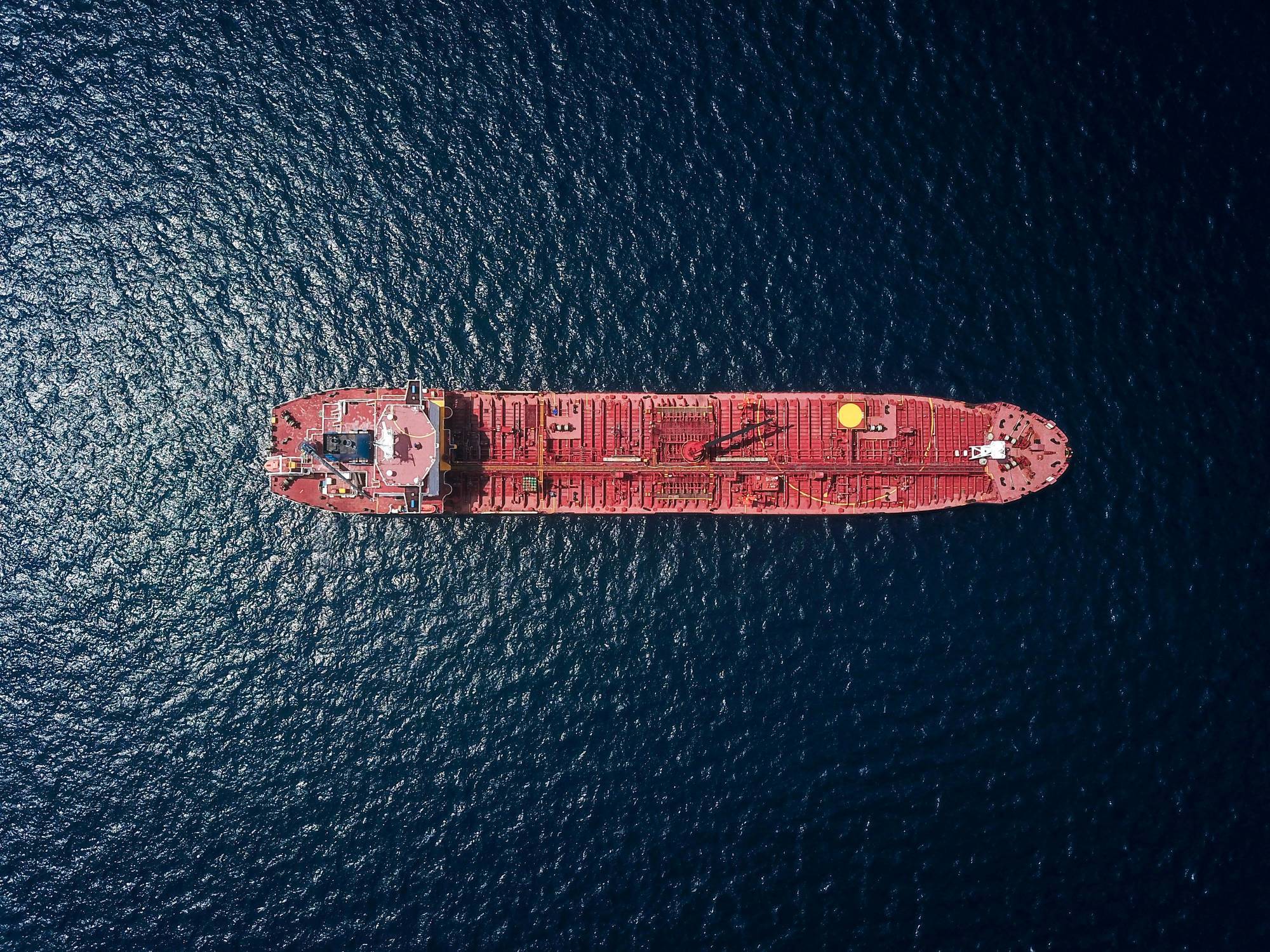 Aerial view of a red cargo ship on deep blue sea.