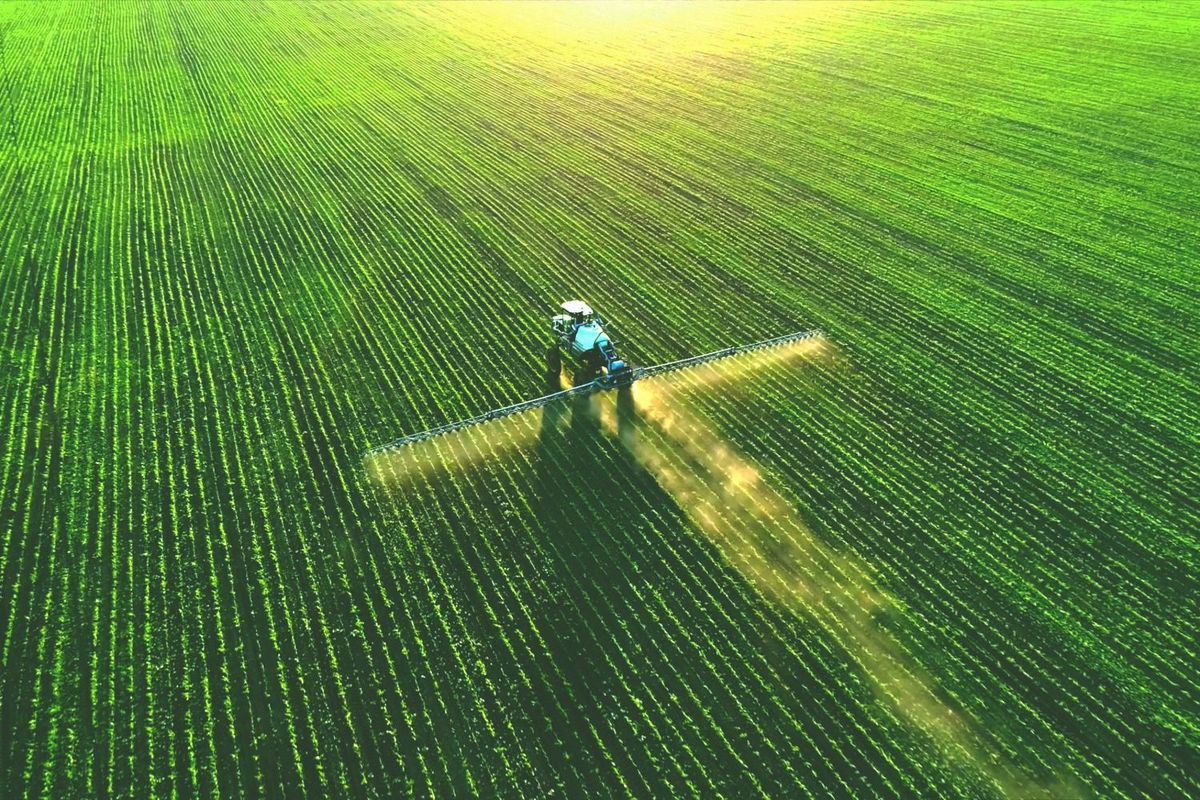 Aerial view of a tractor spraying a vast, green field at sunset.