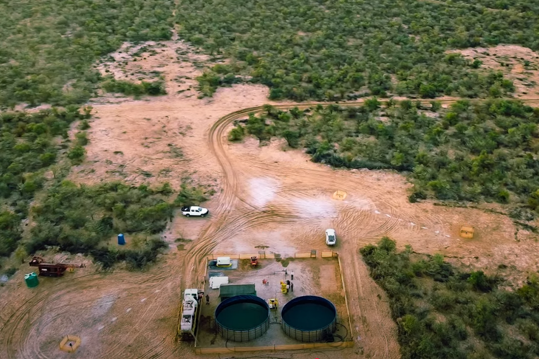 Aerial view of desert landscape with two cars and industrial tanks surrounded by sparse greenery.