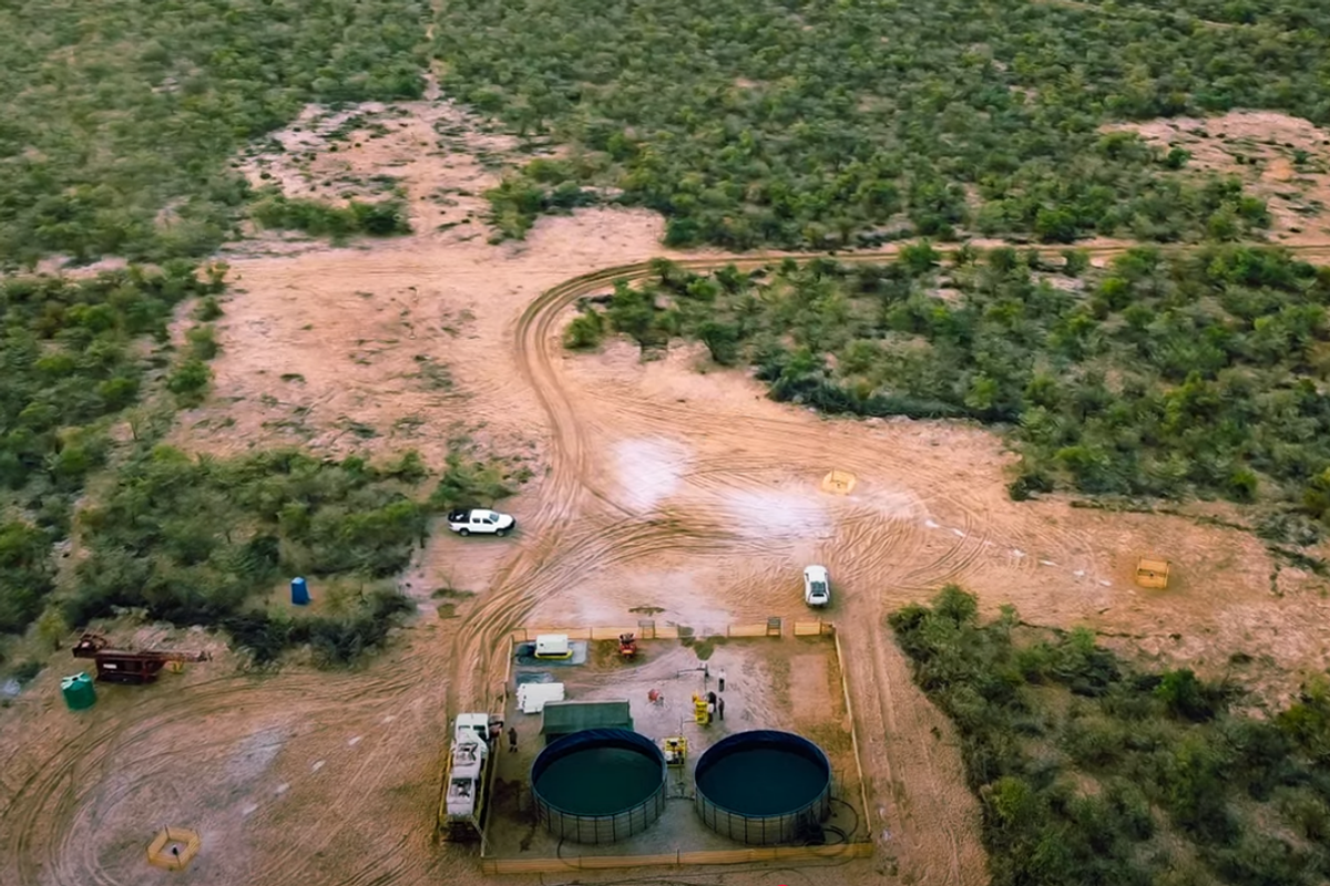 Aerial view of desert landscape with two cars and industrial tanks surrounded by sparse greenery.