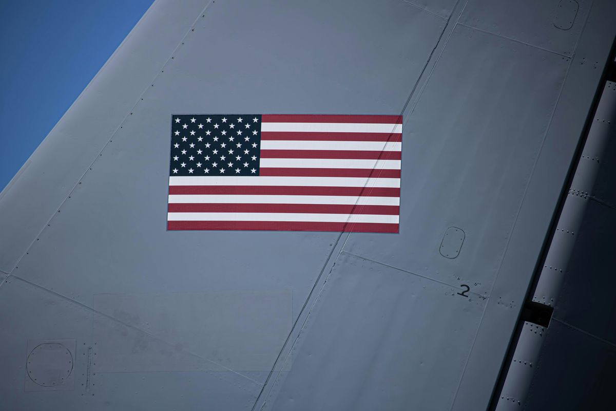 American flag on side of a gray aircraft tail under blue sky.