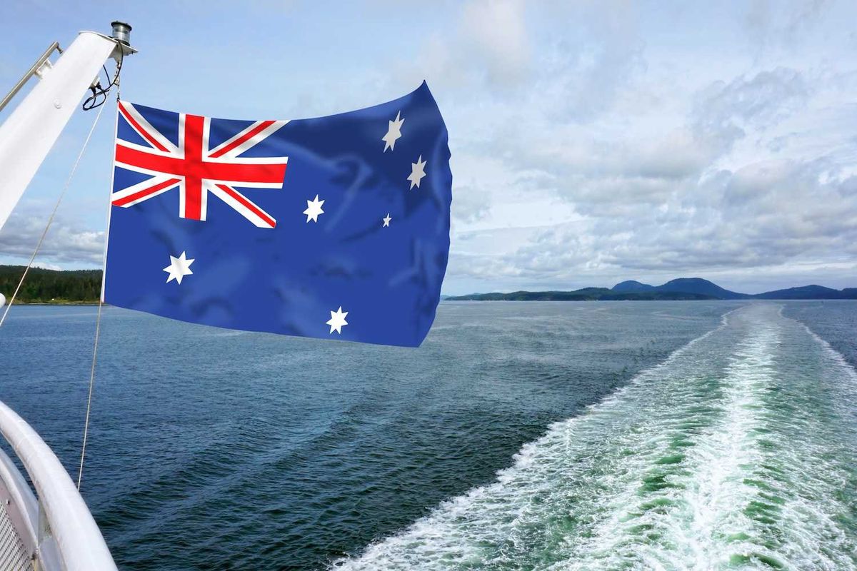 Australian flag on a boat overlooking the sea, with distant mountains under a cloudy sky.
