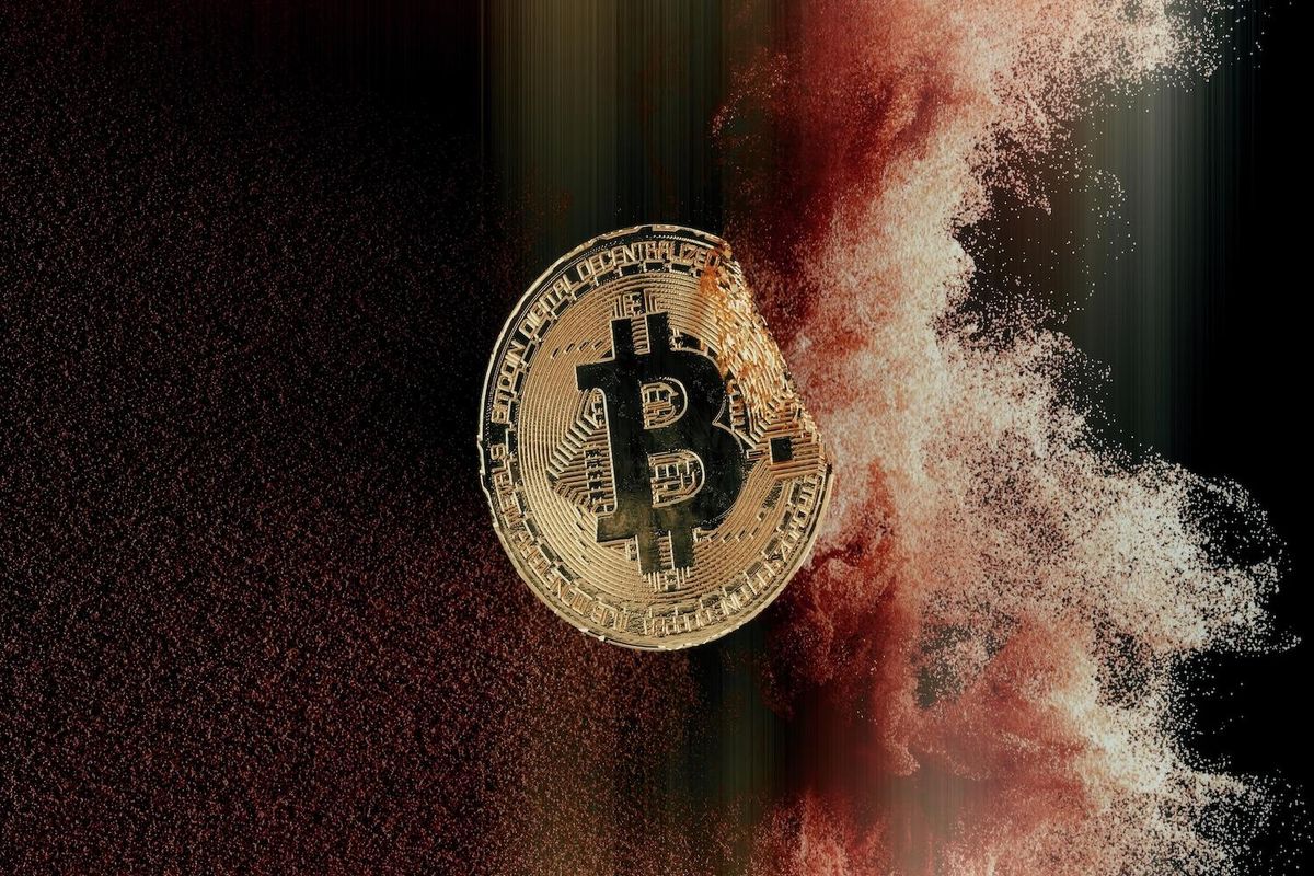 Bitcoin coin disintegrating into particles against a dark background.
