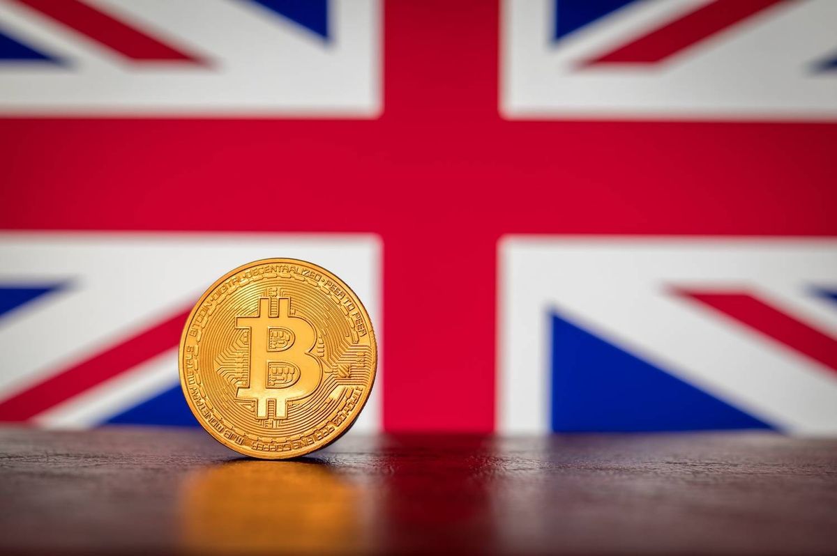 Bitcoin coin on a table against a blurred UK flag background.