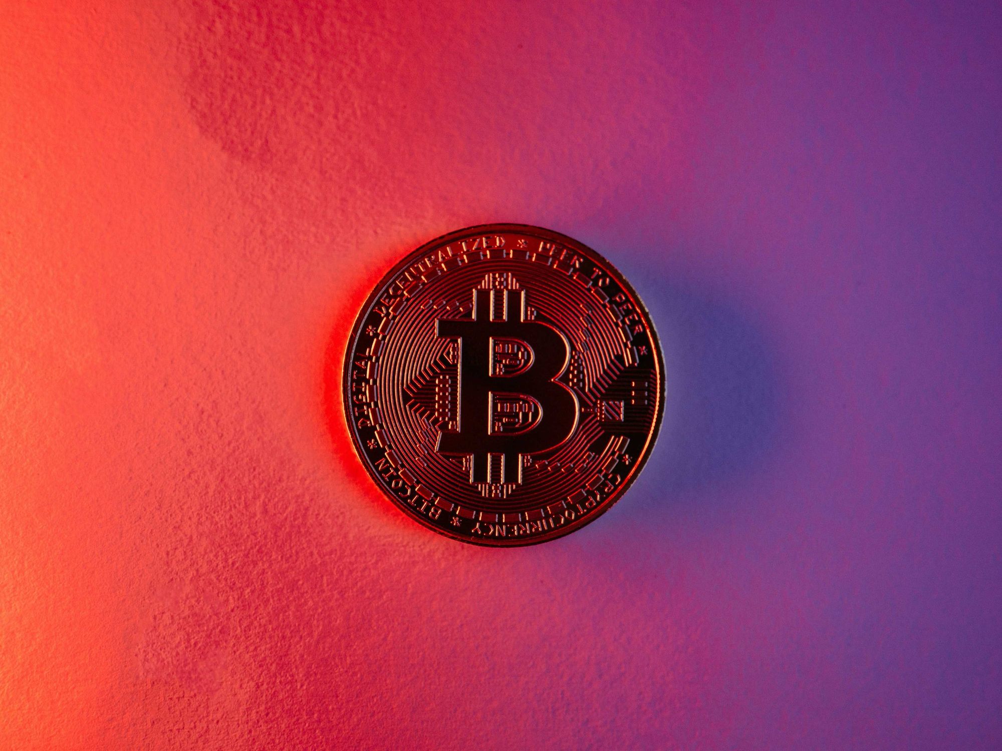 Bitcoin coin on red and purple gradient background.