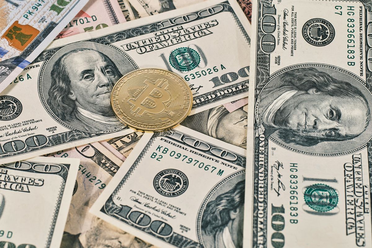 Bitcoin coin on scattered US$100 bills.