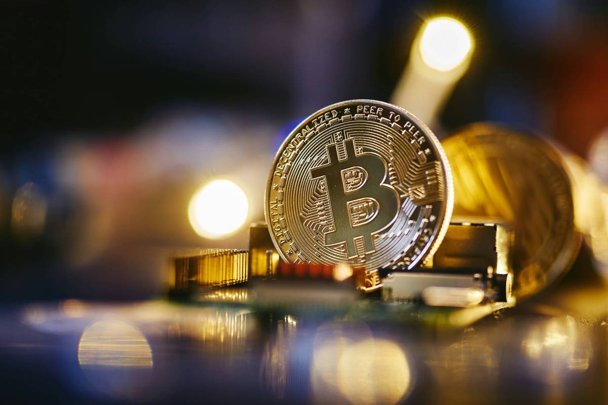 Bitcoin stands upright on a reflective surface with blurred lights in the background.