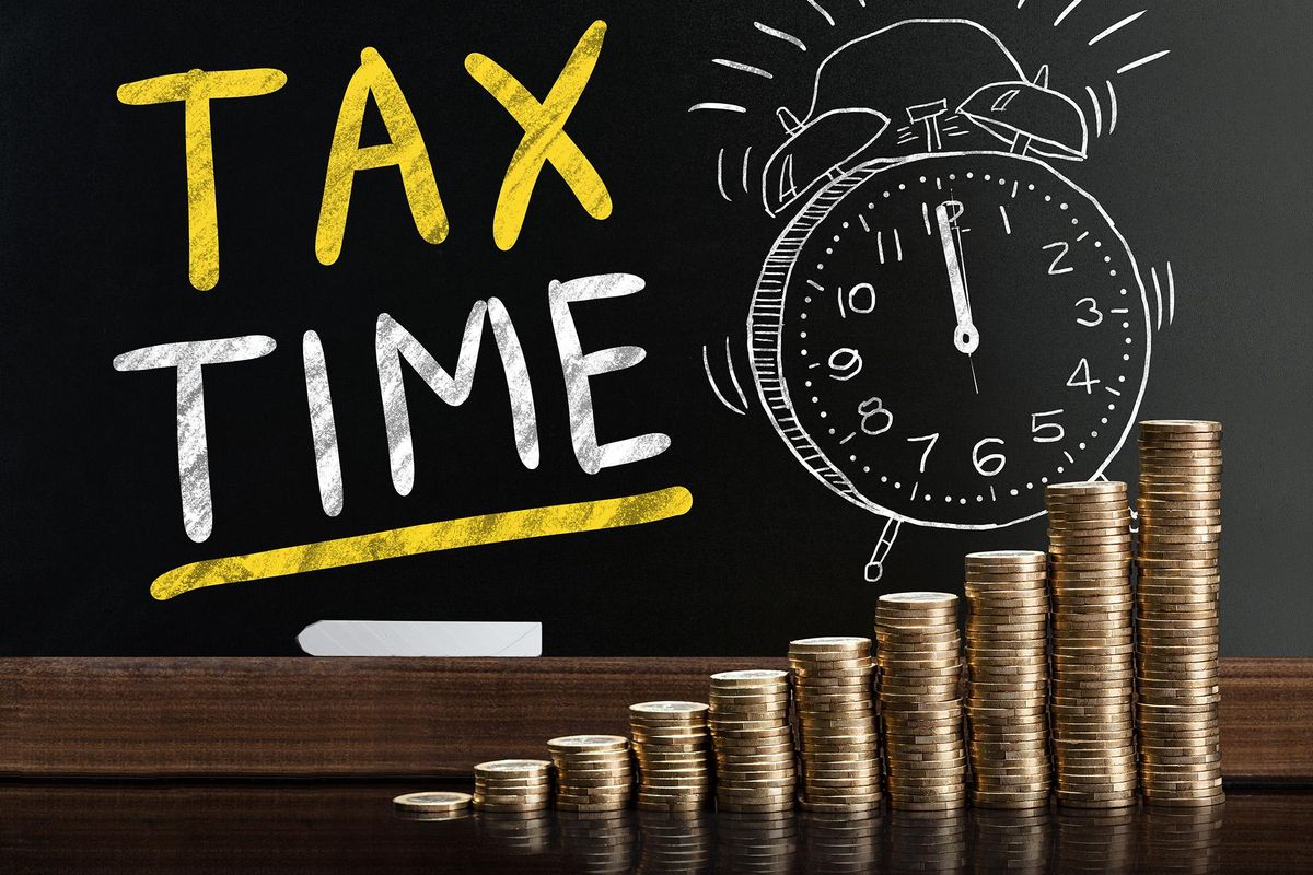 Blackboard with the words "tax time" and alarm clock in front of stacks of pennies.