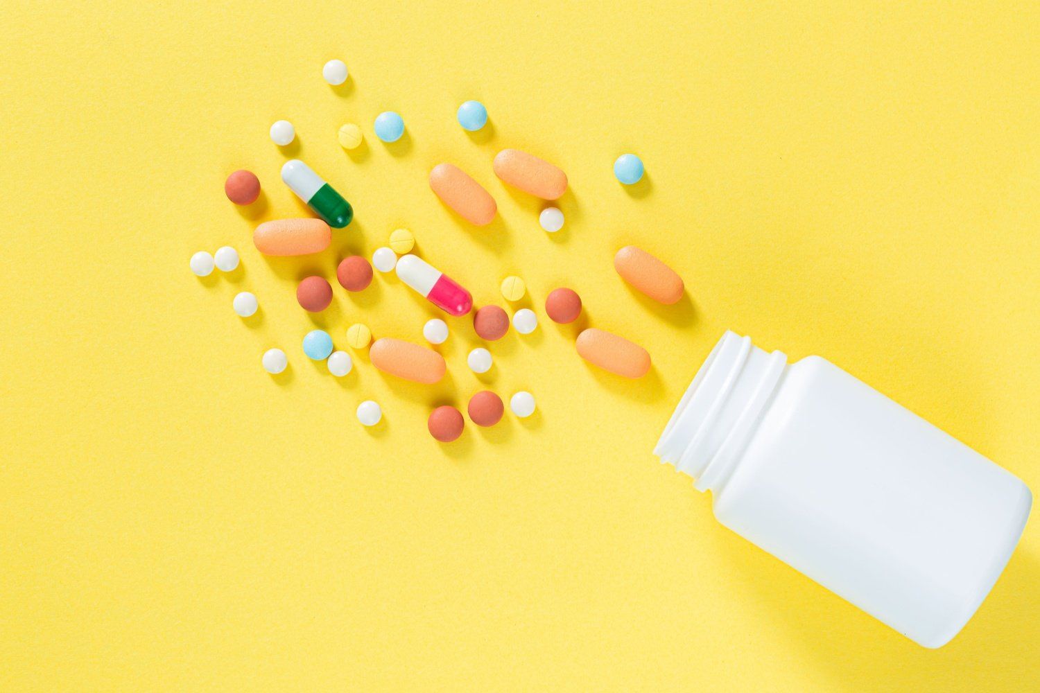 Blank pill bottle spilling a variety of pharmaceutical pills and capsules.