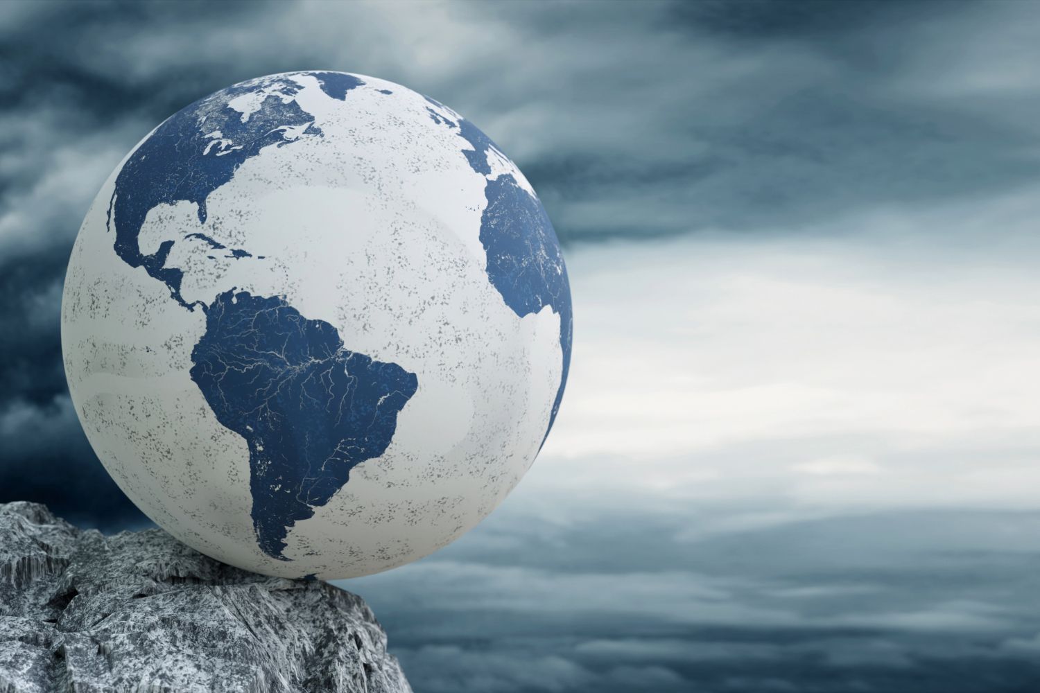 Blue and white globe balancing on a rocky surface with cloudy sky backdrop.