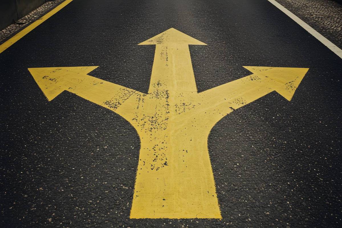 Bold yellow three-directional arrow painted on a textured black asphalt road.