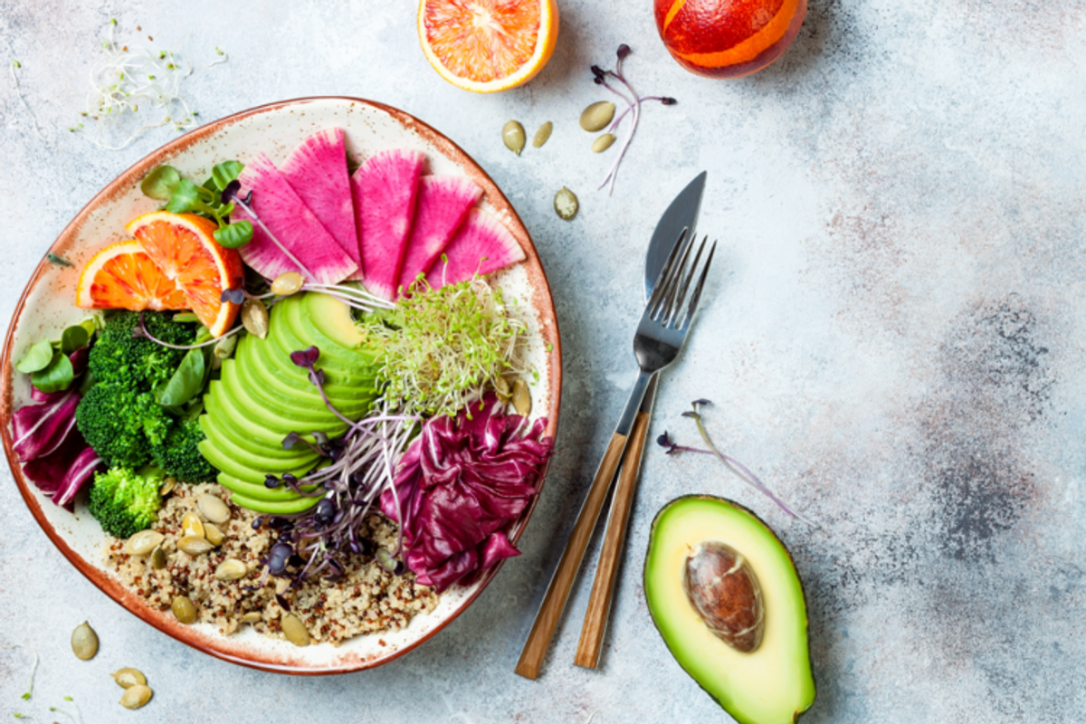 bowl with healthy food on it alongside an avocado and cutlery