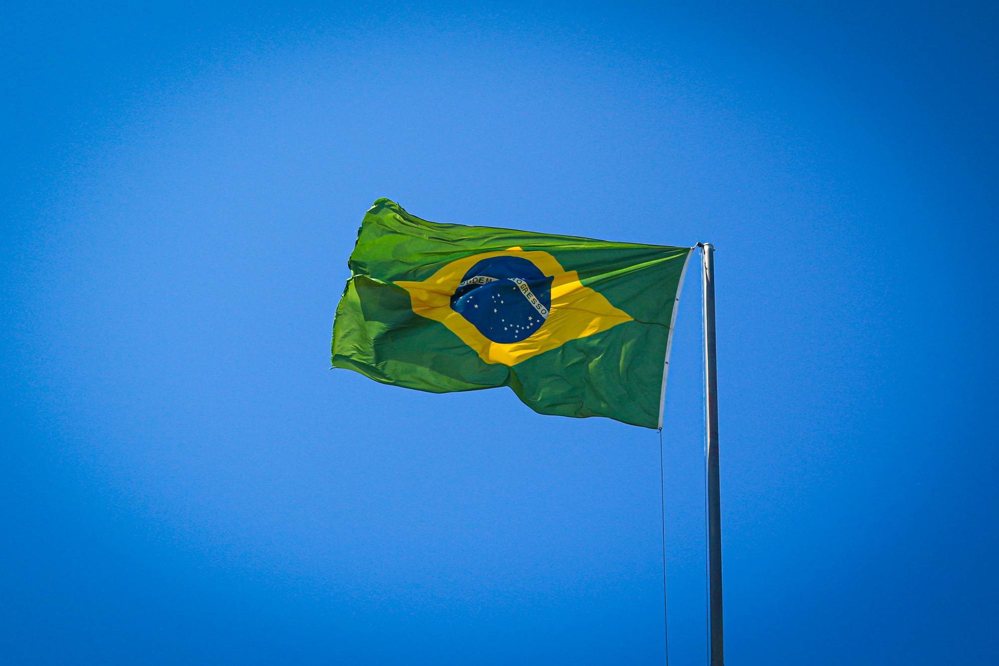 Brazilian flag waving against a clear blue sky.