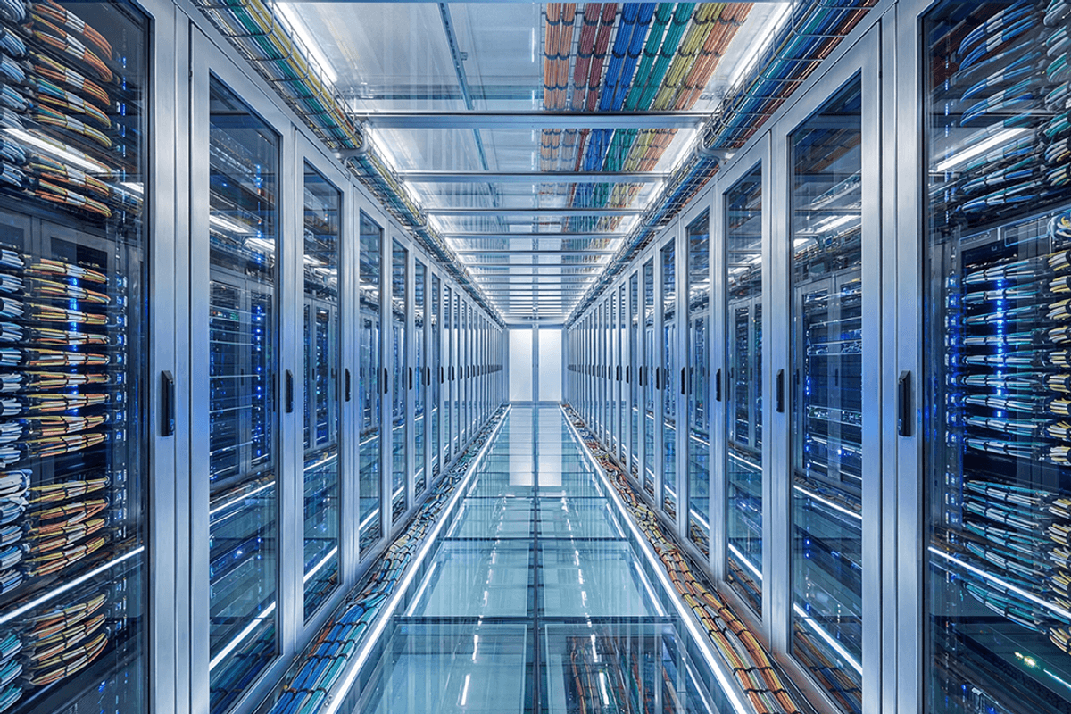 Brightly lit server room with rows of metal racks on shiny floors and colorful cables overhead.
