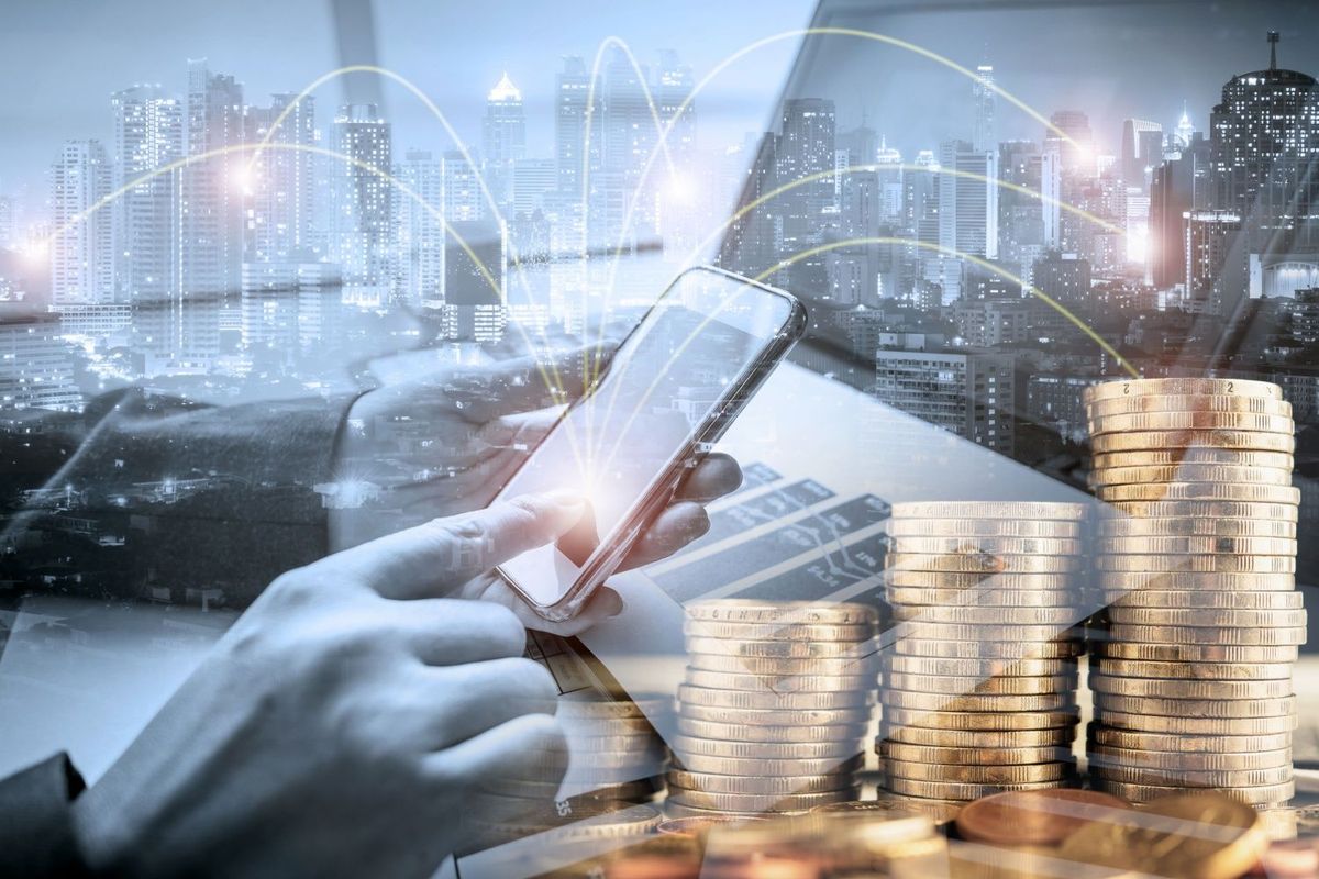 Businessperson holding cell phone with laptop and gold coins.